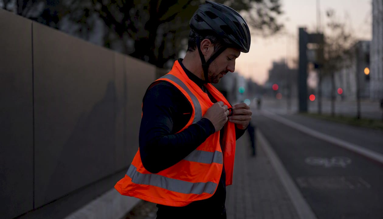 Un cycliste ajuste son gilet fluorescent pour être bien visible en pleine journée.