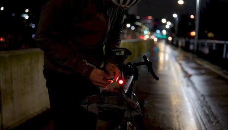 Un cycliste règle son éclairage avant alors que la nuit commence à tomber.