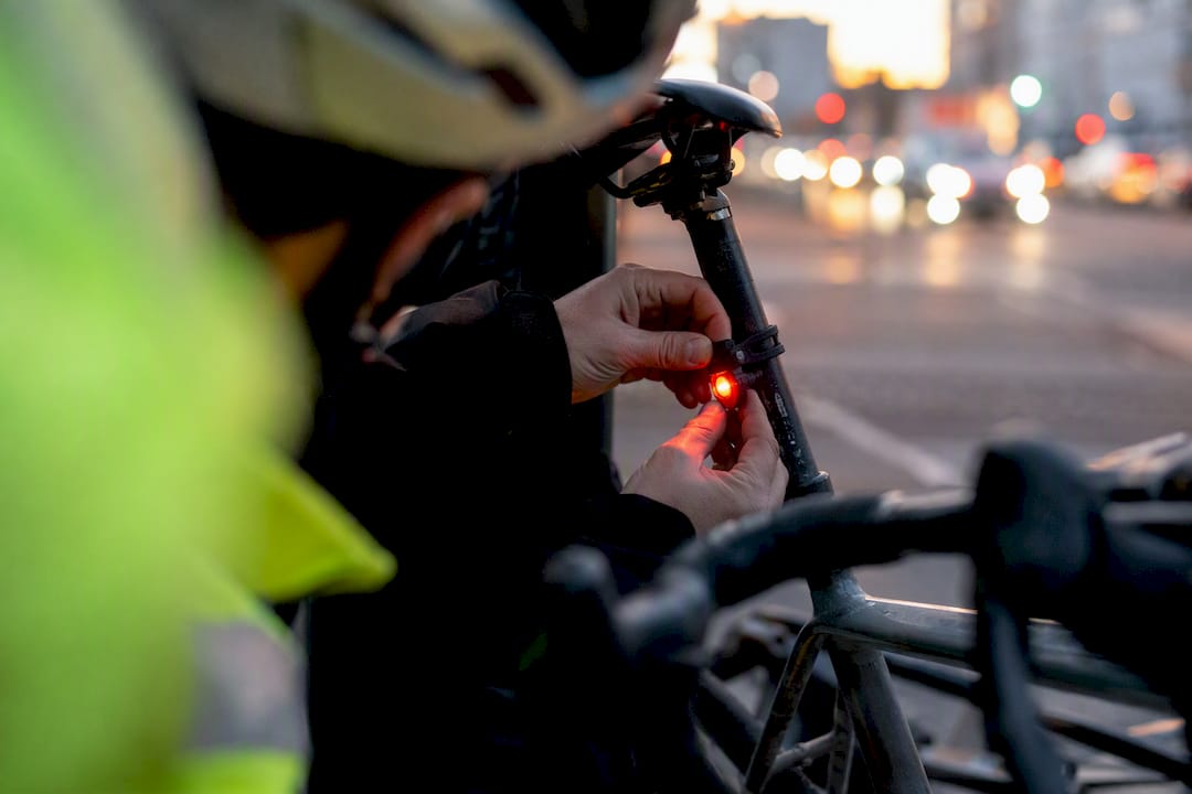 Un cycliste règle son feu arrière alors que la nuit commence à tomber.