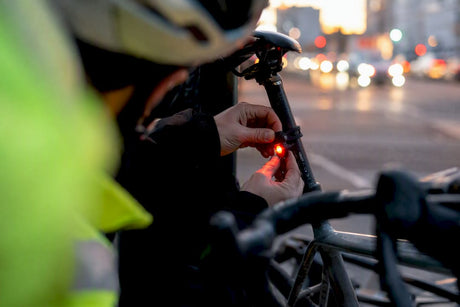 Un cycliste règle son feu arrière alors que la nuit commence à tomber.